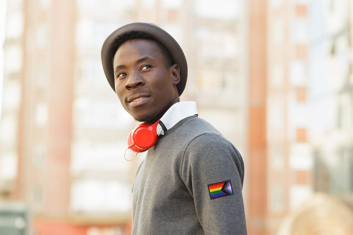 a young African American man wearing a shirt with lgbtq+ flag patch on the sleeve